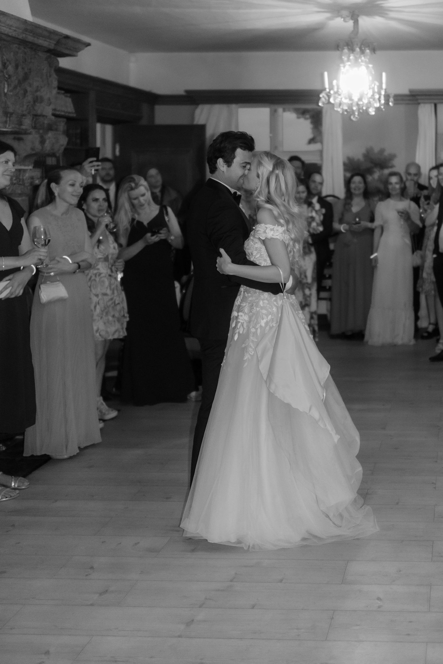 Wedding guests watch as the couple performs their first dance under a crystal chandelier.