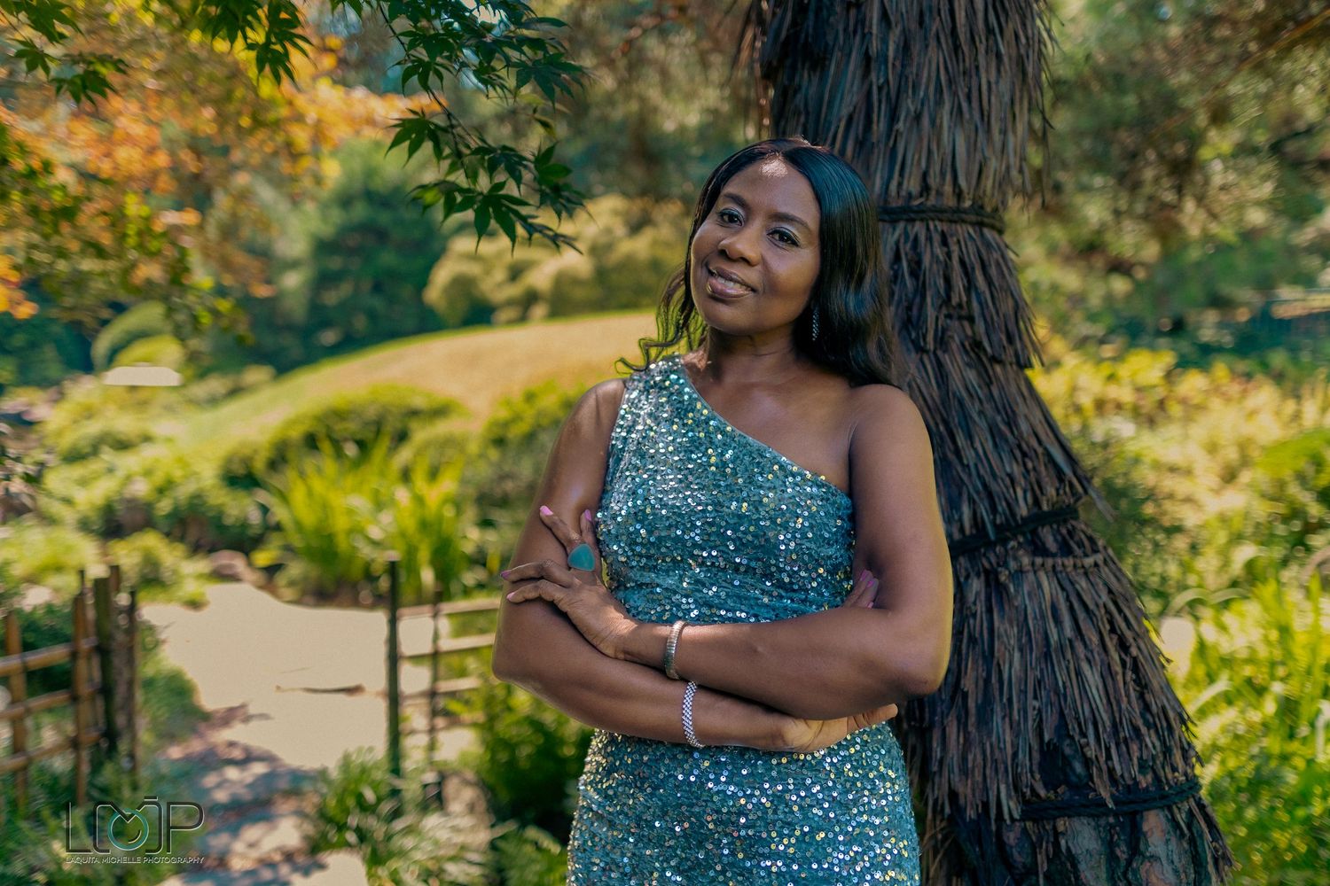 Sparkling teal evening gown photographed in a lush outdoor garden setting.
