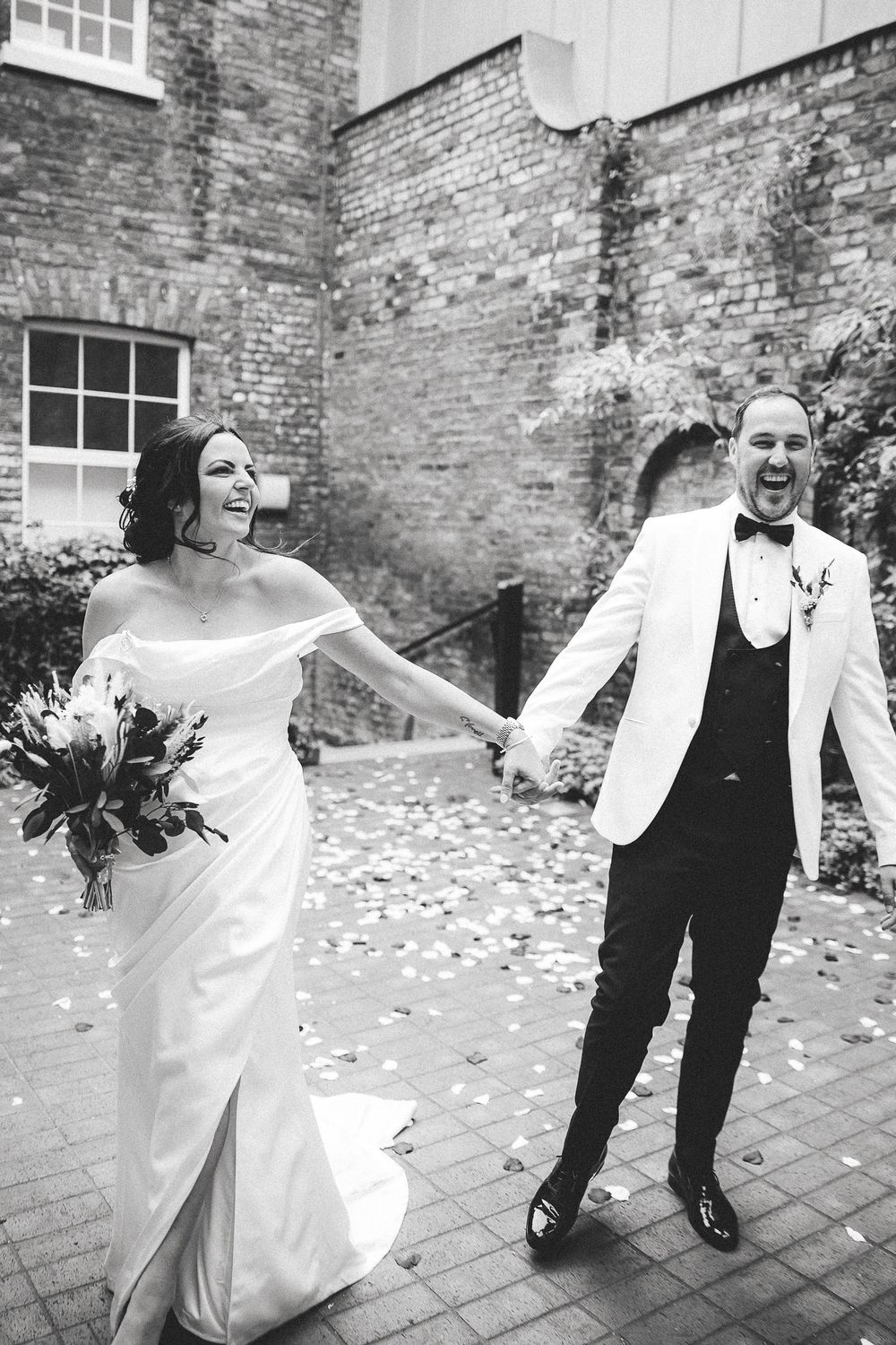 A joyful newlywed couple share a candid moment on their wedding day outside a historic brick building.