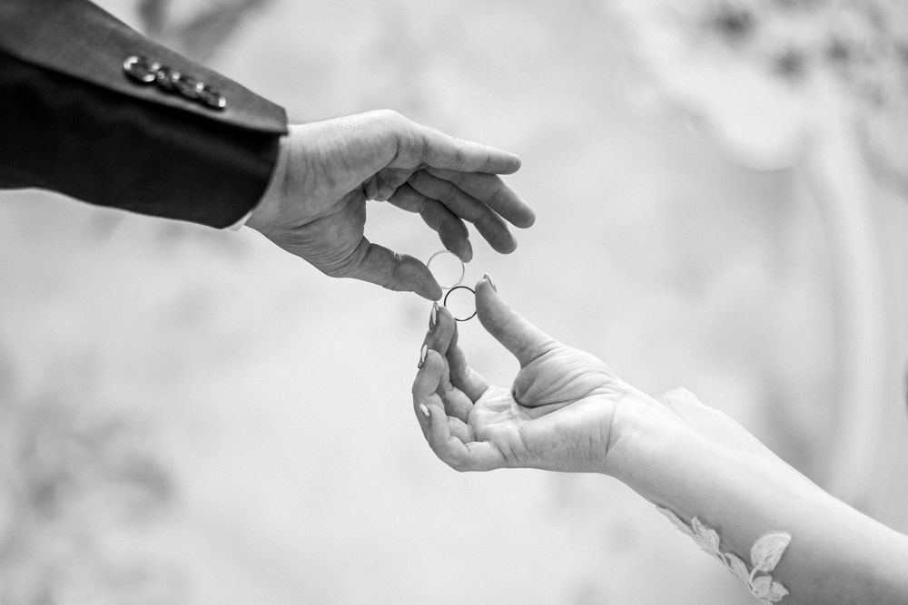 A black and white photo of two hands exchanging a wedding ring during a ceremony.
