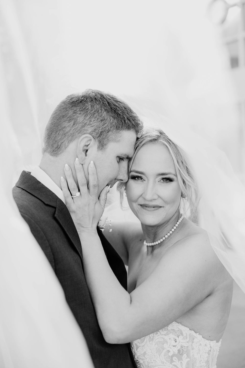 Intimate black and white wedding portrait showing tender moment between newlyweds in formal attire.