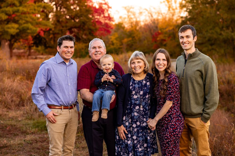 A family portrait taken at sunset during autumn with colorful fall foliage in the background.
