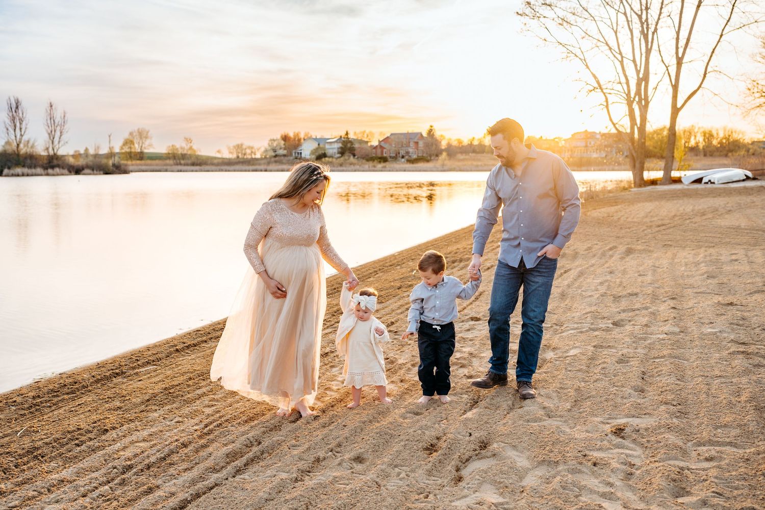 A family walks along a sandy beach shore at sunset beside a calm lake, creating a peaceful outdoor scene together.