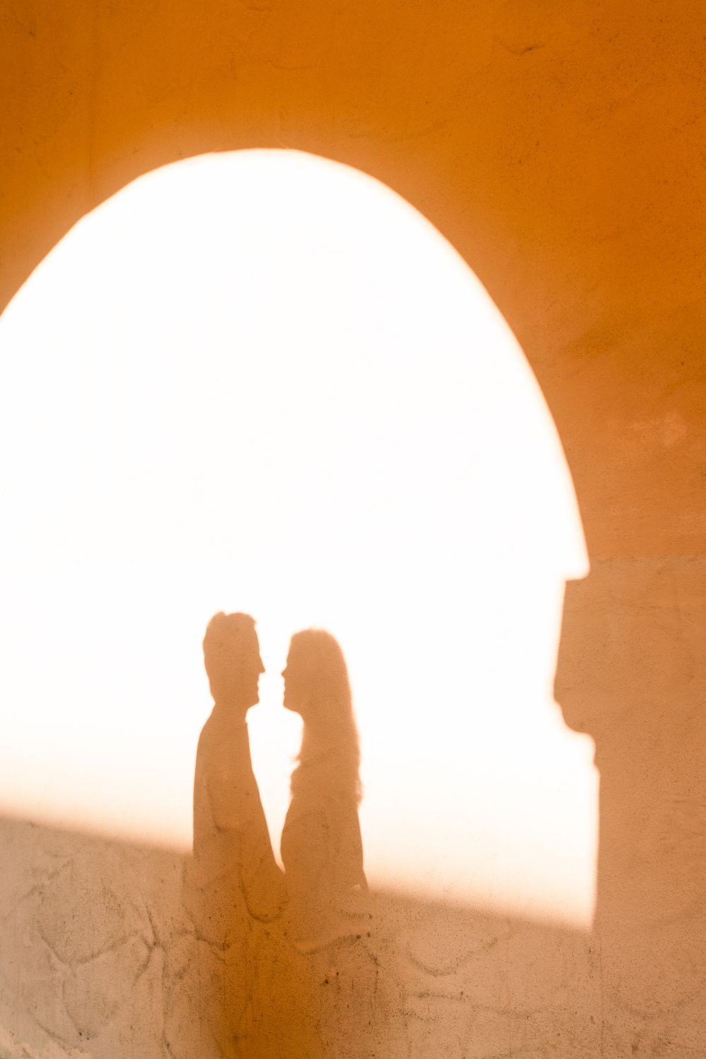 Silhouettes of a couple standing in an arched doorway at sunset creating a romantic sepia-toned scene.