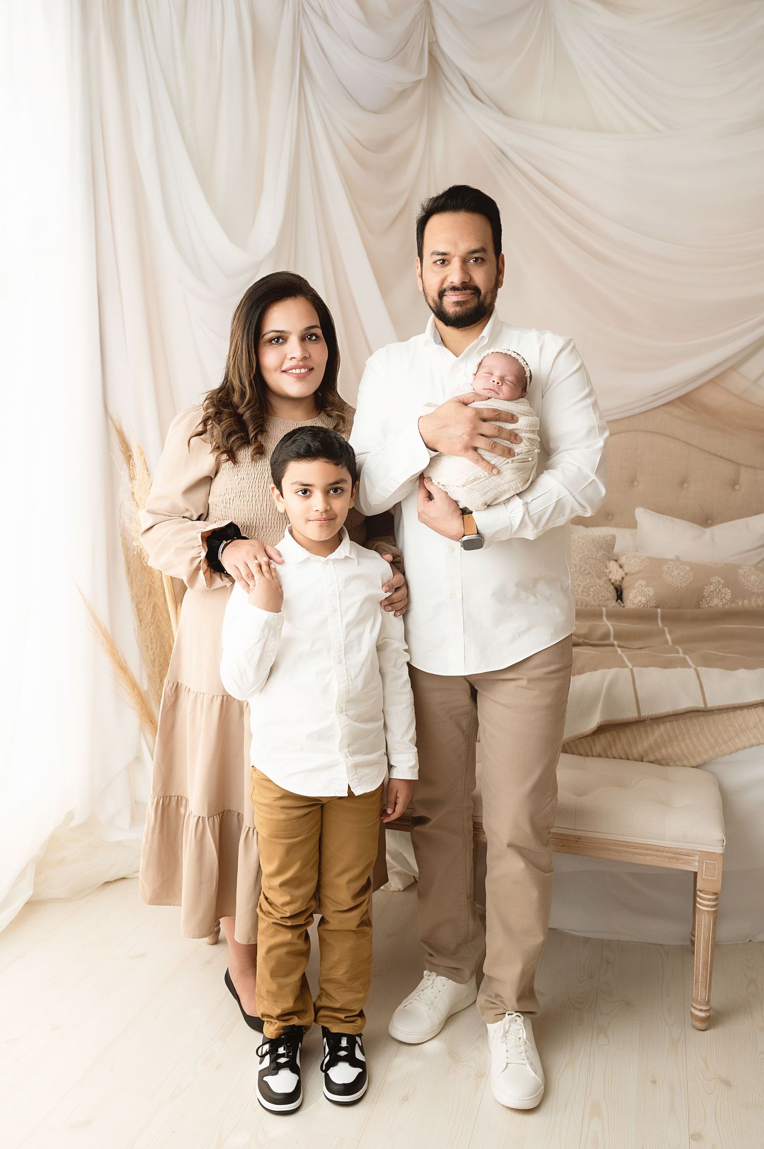 Family portrait with coordinated outfits against white draped background.
