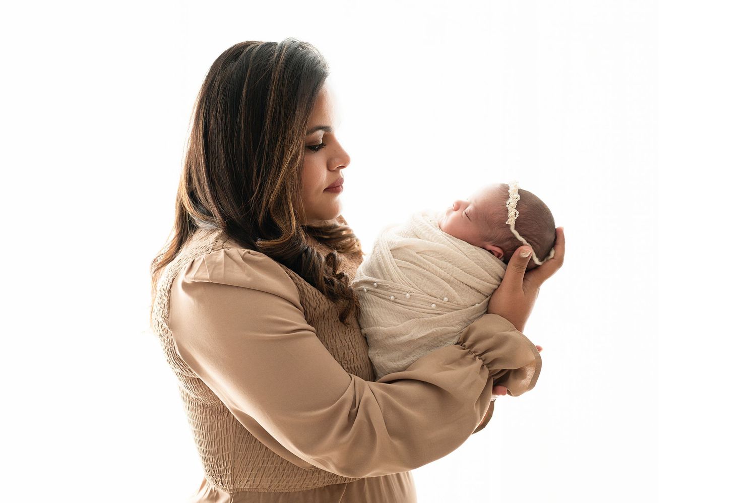 Family in coordinated neutral outfits poses against white background in minimalist studio setting.