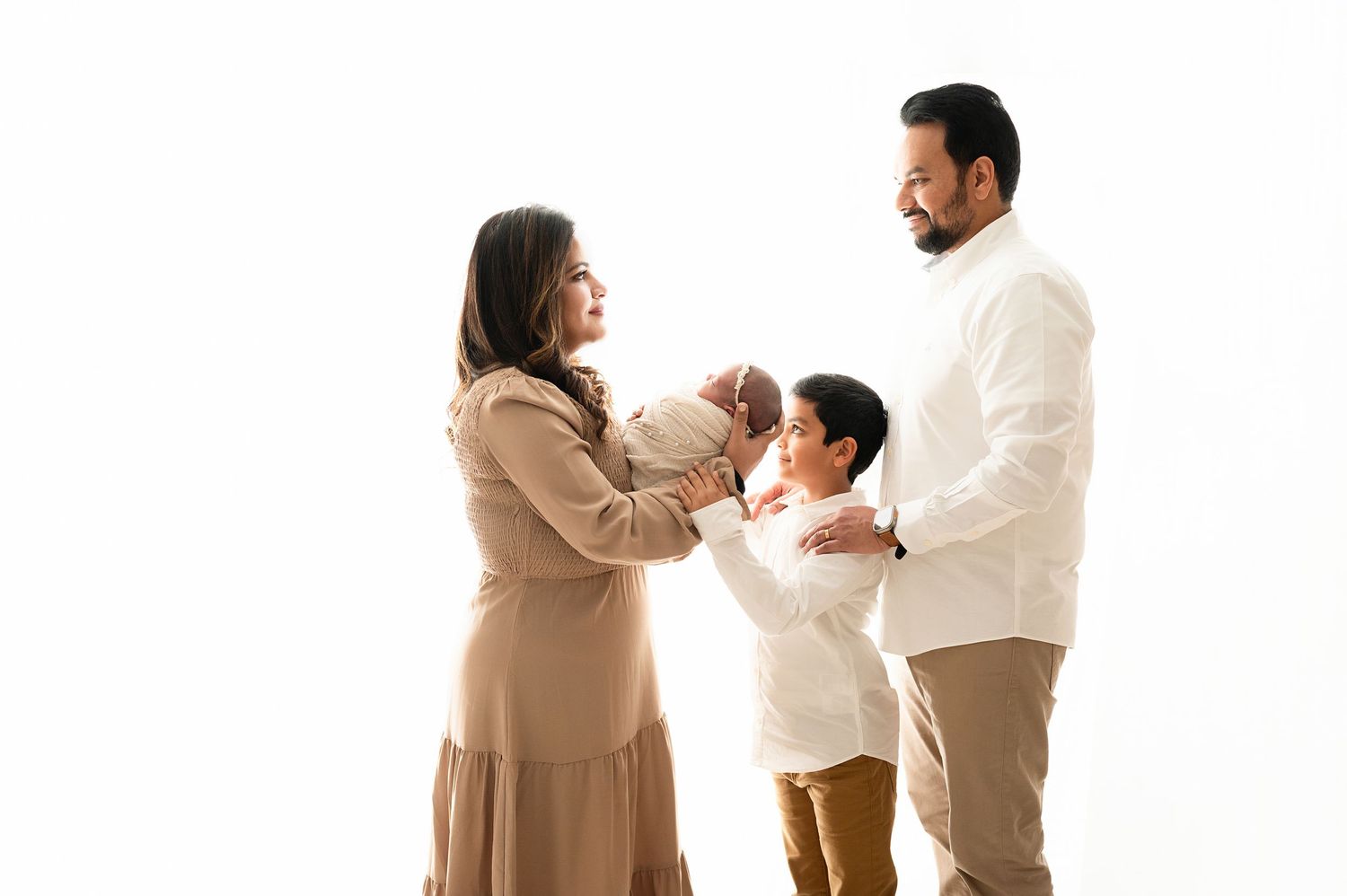 A family wears matching beige and white outfits while posing together in a studio.
