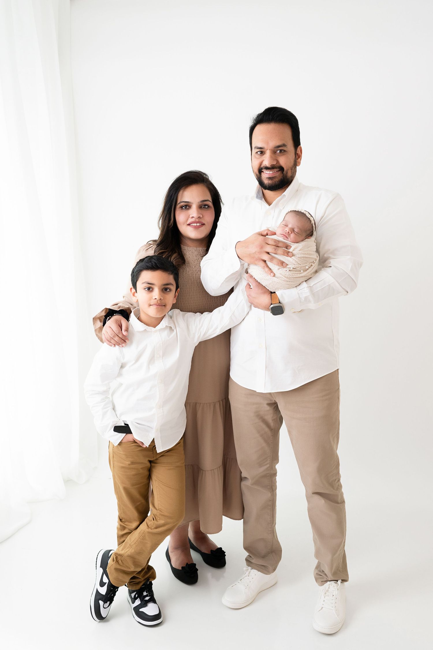 Family members in coordinated beige and white attire interact playfully in bright studio setting.