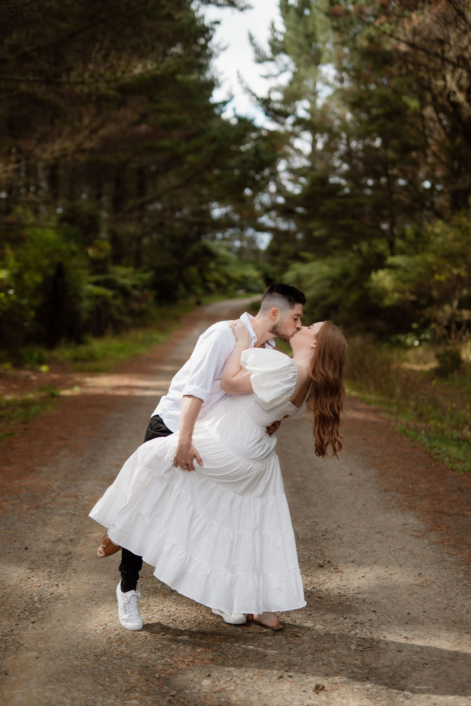 A newlywed couple shares a romantic dip kiss in front of a mint green vintage car in a grassy meadow.