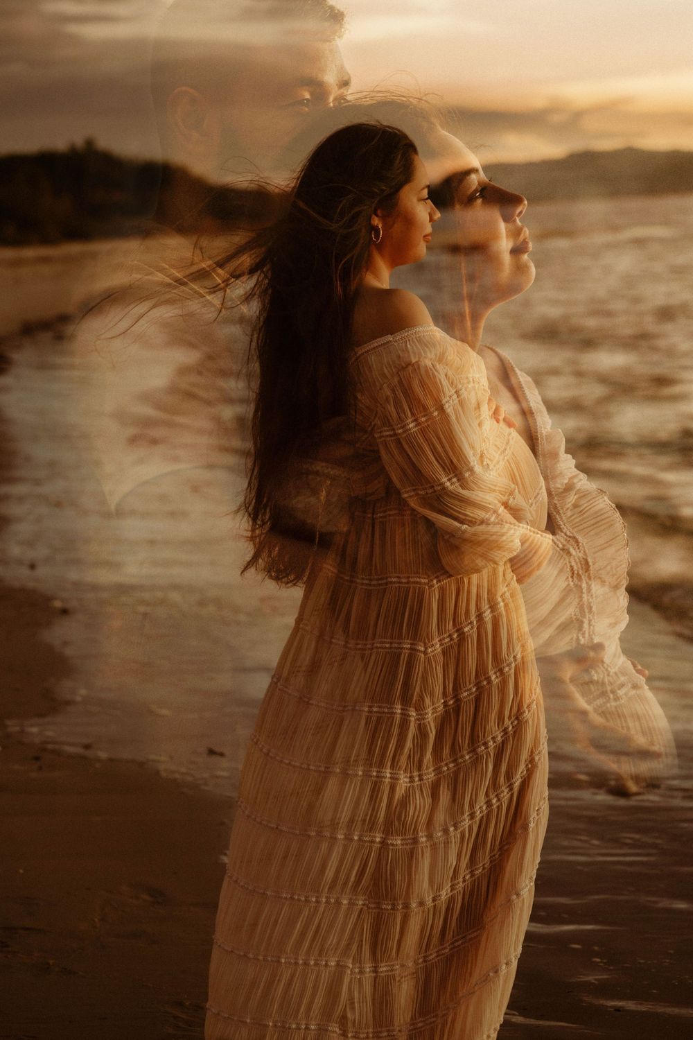 Figure in a flowing white vintage dress stands by the ocean at golden hour with wind-swept hair and dreamy lighting.