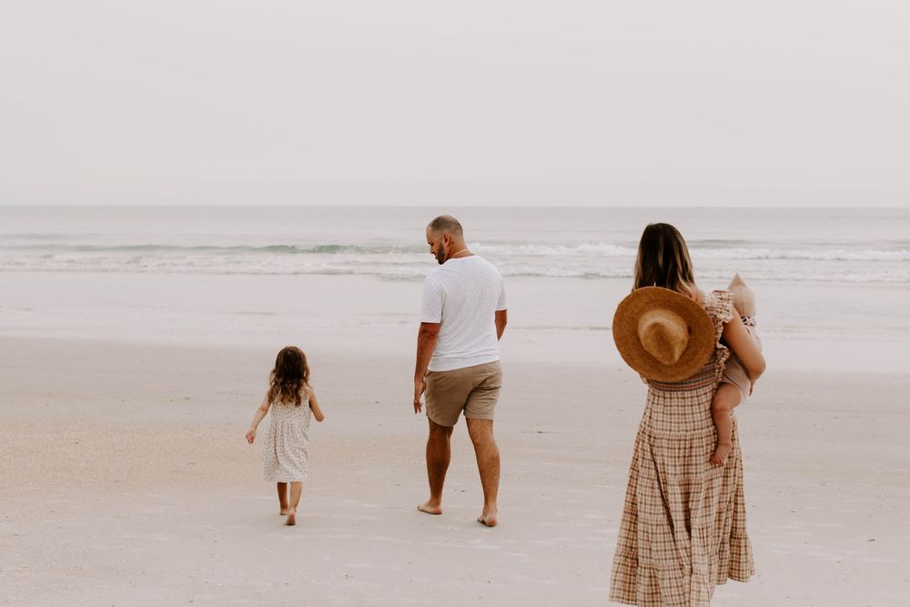 Family strolling along empty beach shoreline during golden hour.