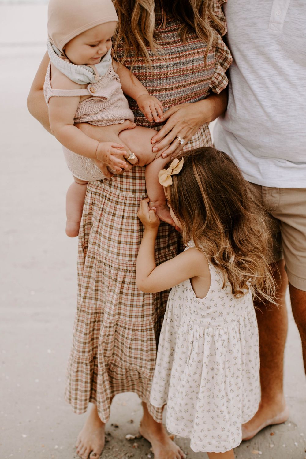 Intimate family moment on beach with children in summer outfits.