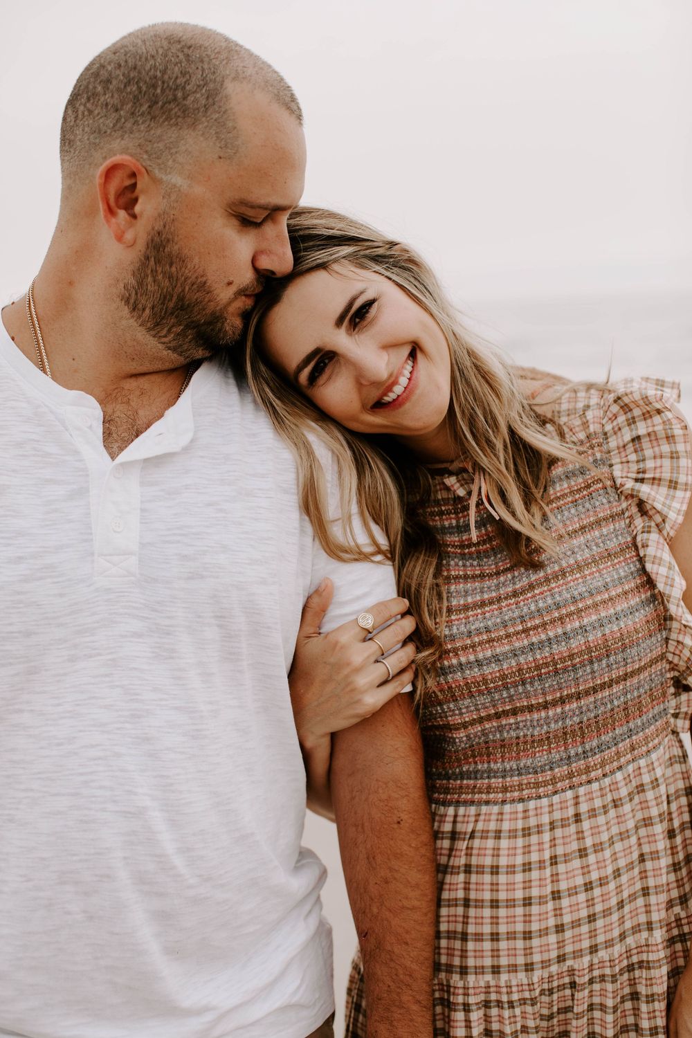 A couple embraces tenderly on the beach against a bright white background.