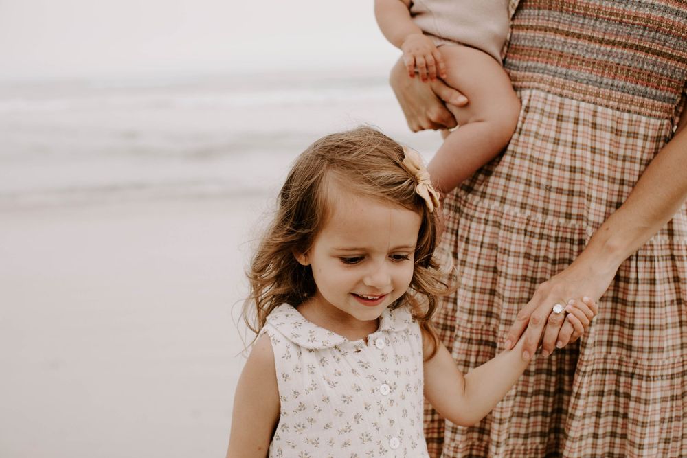 Family wearing coordinated neutral outfits poses together at the beach.