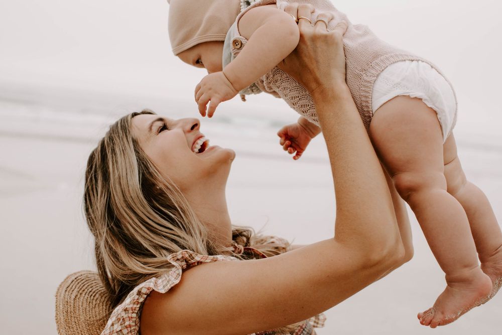 Parent joyfully lifts laughing baby in the air at seaside.