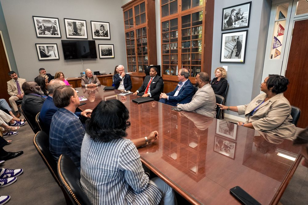 Business professionals gathered around a large conference table in a room adorned with black and white photographs.