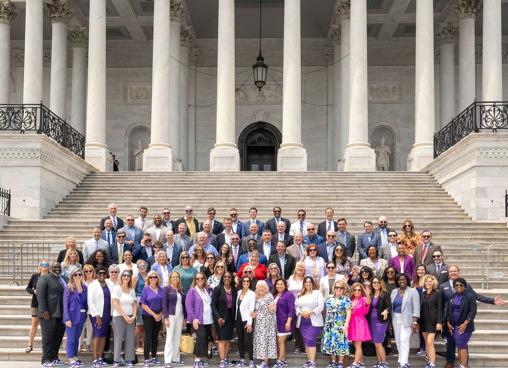 Large group of people gathered on the steps of the U.S. Capitol building with white columns in the background.
