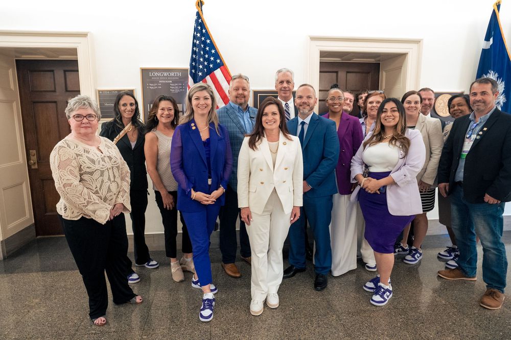 A group of people gathered in a hallway near American flags and office doors.