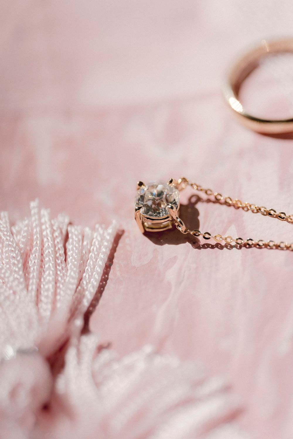 Delicate rose gold jewelry chain with gems lies softly against blush pink fur or fabric texture in soft lighting.