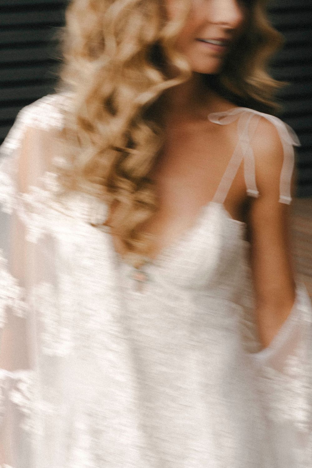 A blurred artistic motion shot showing flowing blonde curls and a white bridal gown with delicate lace details.