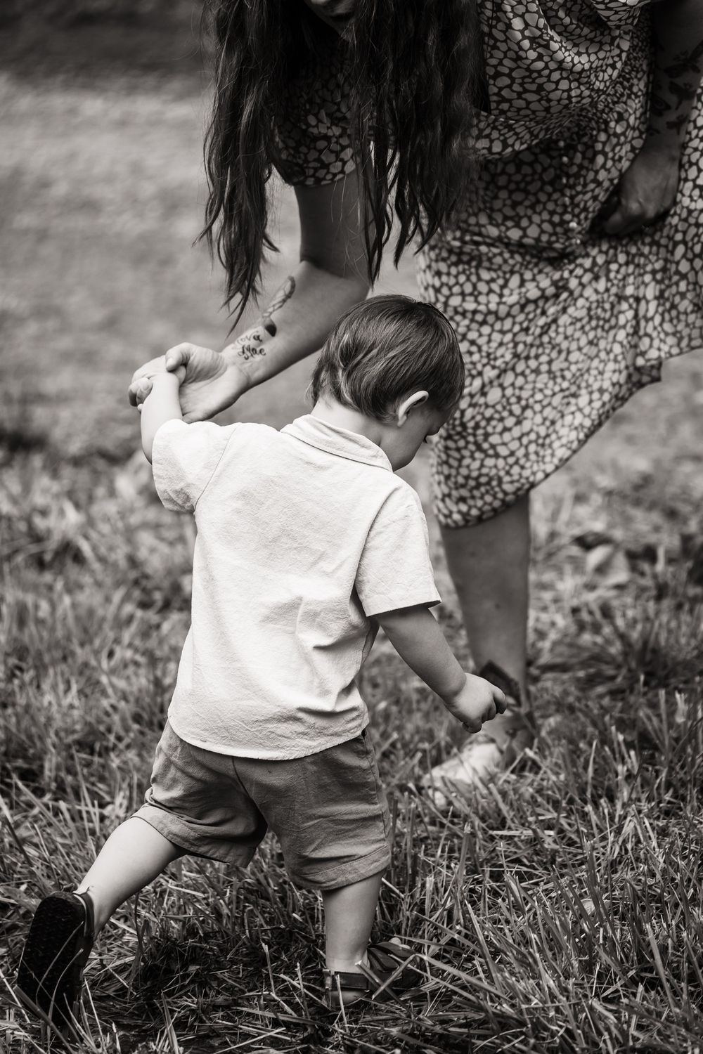 Black and white image of a small child playing in tall grass while wearing a white shirt.