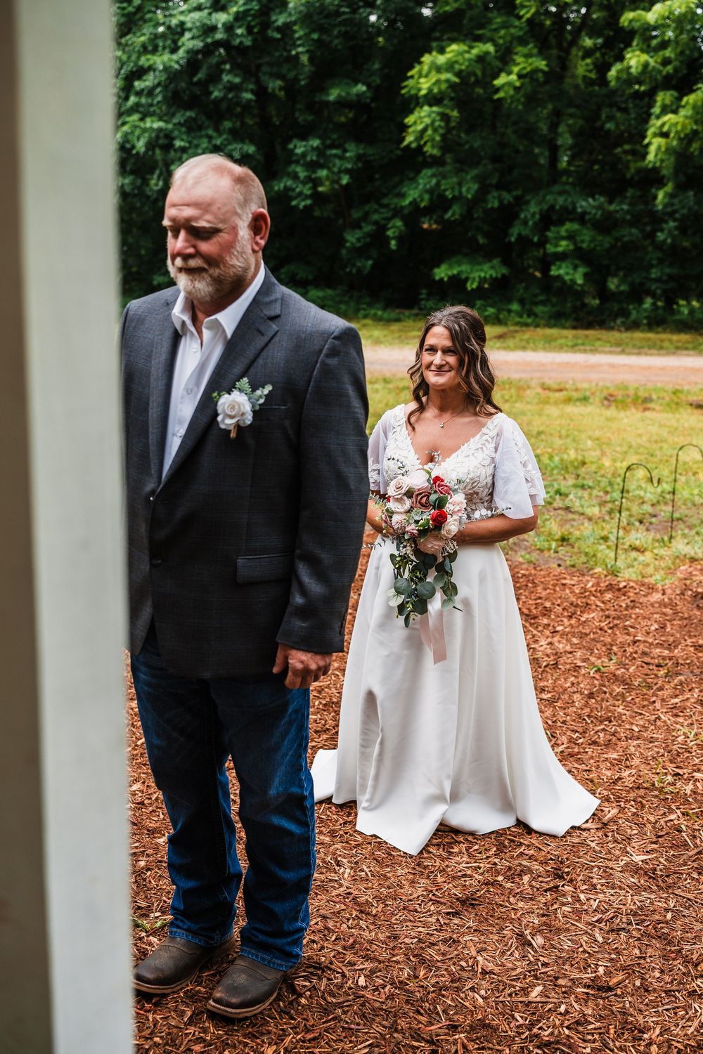 Wedding portrait in front of trees with bride holding bouquet and wearing flowing white dress.