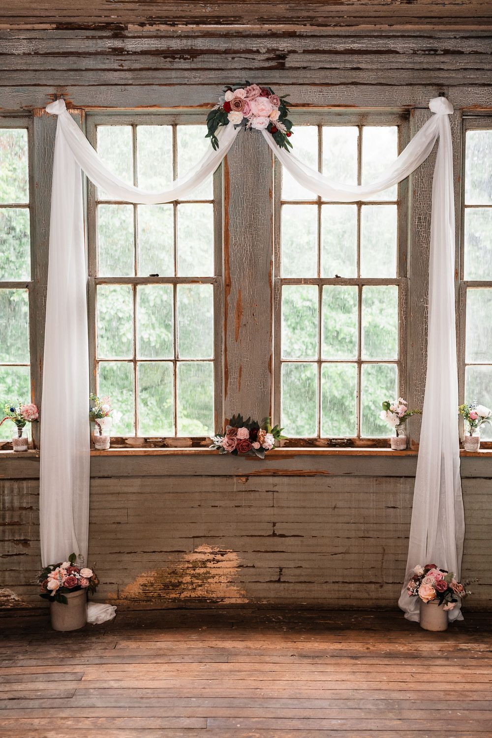 Rustic indoor venue with white drapes and wooden floors illuminated by natural window light.