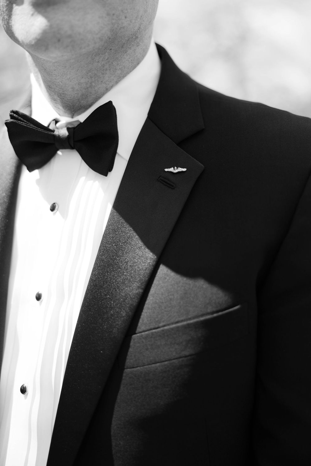 Close-up black and white photo of formal tuxedo with black bow tie and white dress shirt with decorative lapel pin.