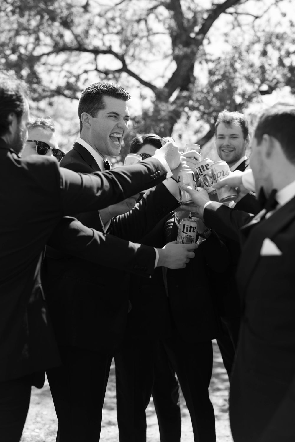 Black and white photo of a group in formal suits celebrating and toasting with bottles outdoors.