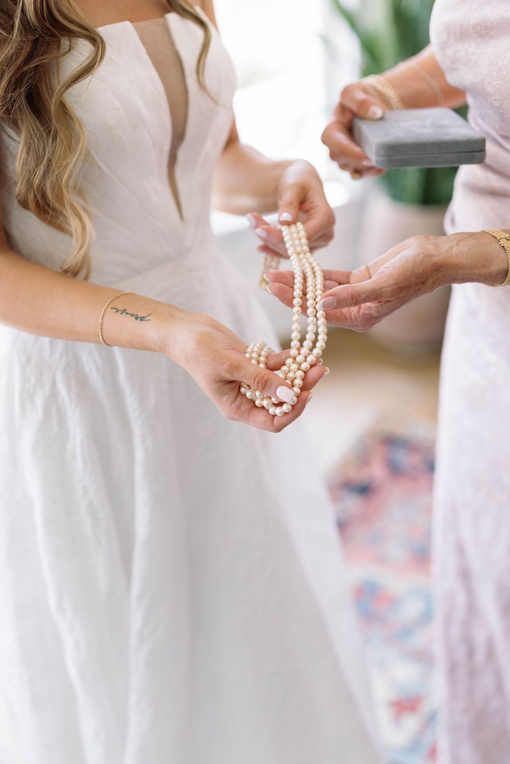 A close-up of hands holding delicate pearl necklaces against a white wedding dress backdrop.