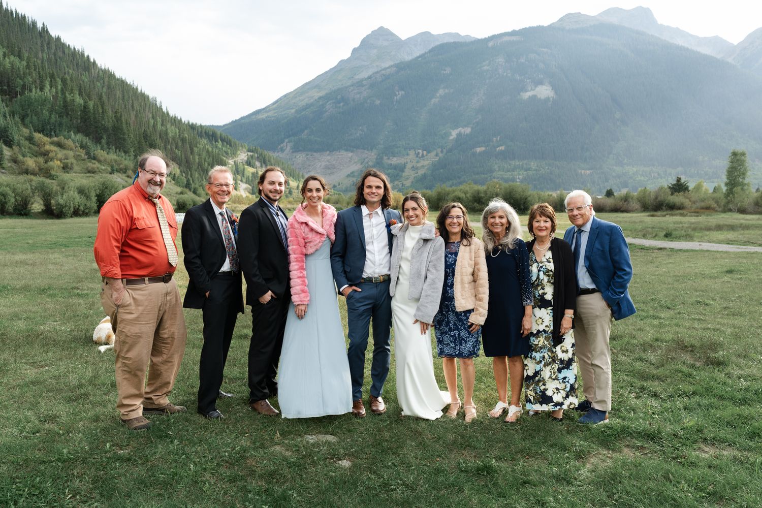 Wedding group photo with family members against mountainous landscape.