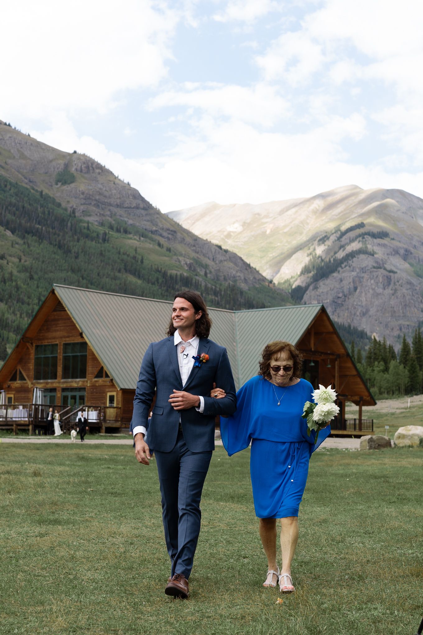 Outdoor wedding ceremony with rustic log cabins and mountain peaks creating a stunning backdrop in the wilderness.