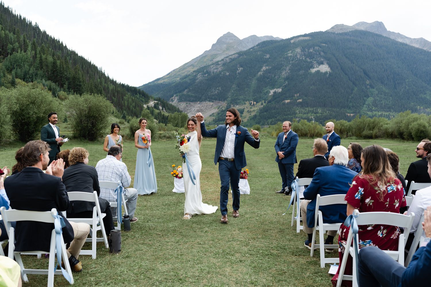 Joyful celebration during outdoor mountain wedding ceremony with guests seated on white chairs.