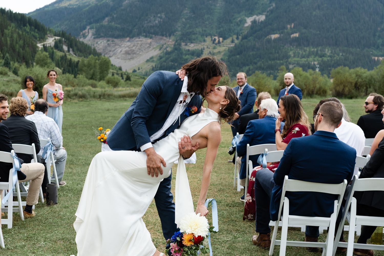 Romantic dip kiss during recessional at outdoor mountain wedding with seated guests.
