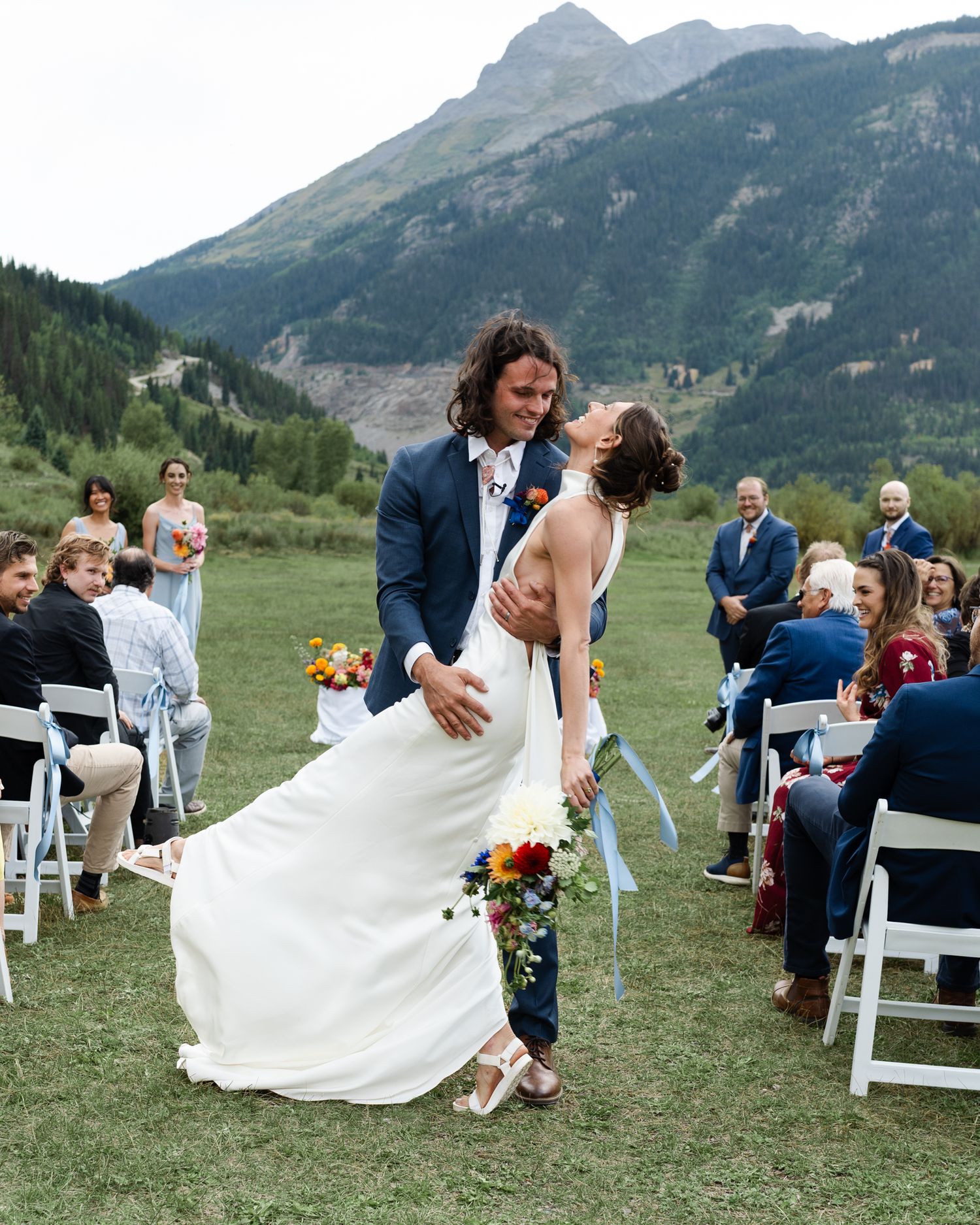 A romantic wedding ceremony takes place outdoors with a stunning mountain backdrop in a scenic valley setting.