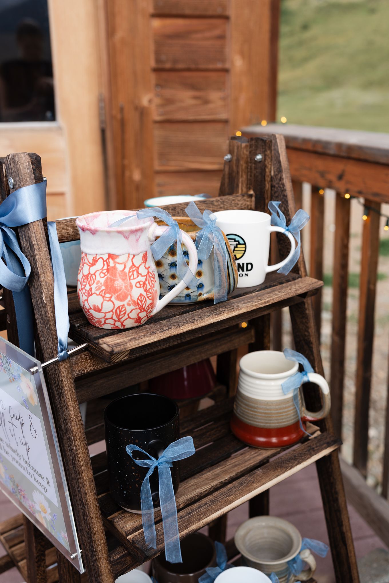 Rustic wooden shelves display mugs and cups decorated with blue ribbons at a wedding reception.