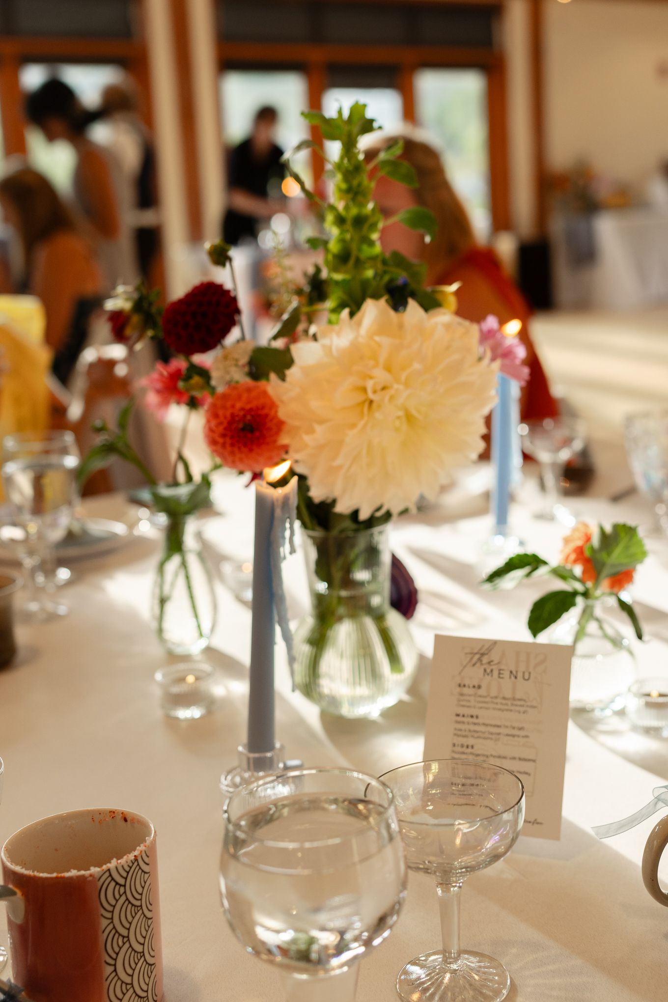 Wedding reception table setting with dahlia floral centerpiece and pale blue candles.