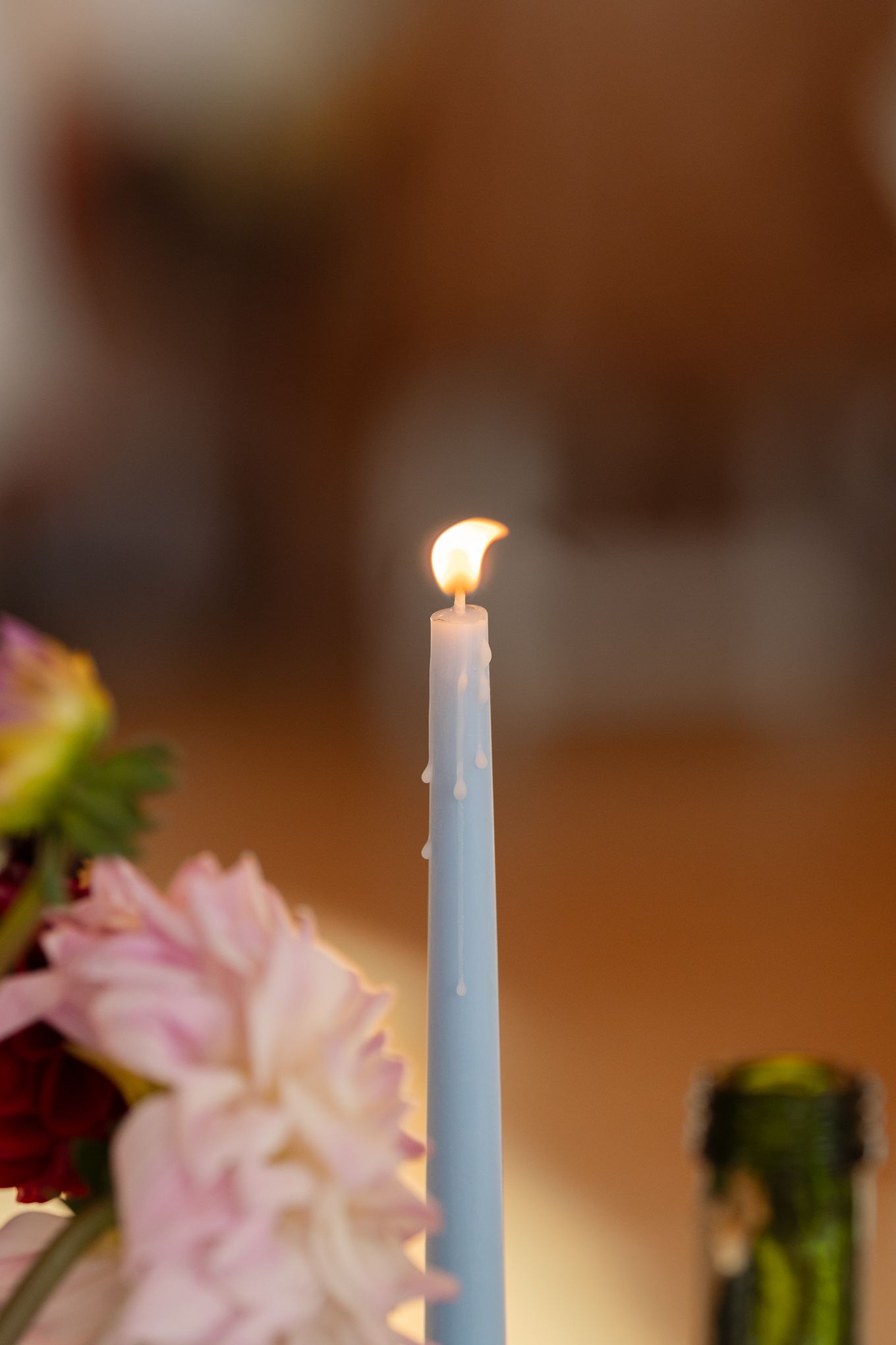 Close-up of a lit pale blue taper candle with soft focus flowers in the background.