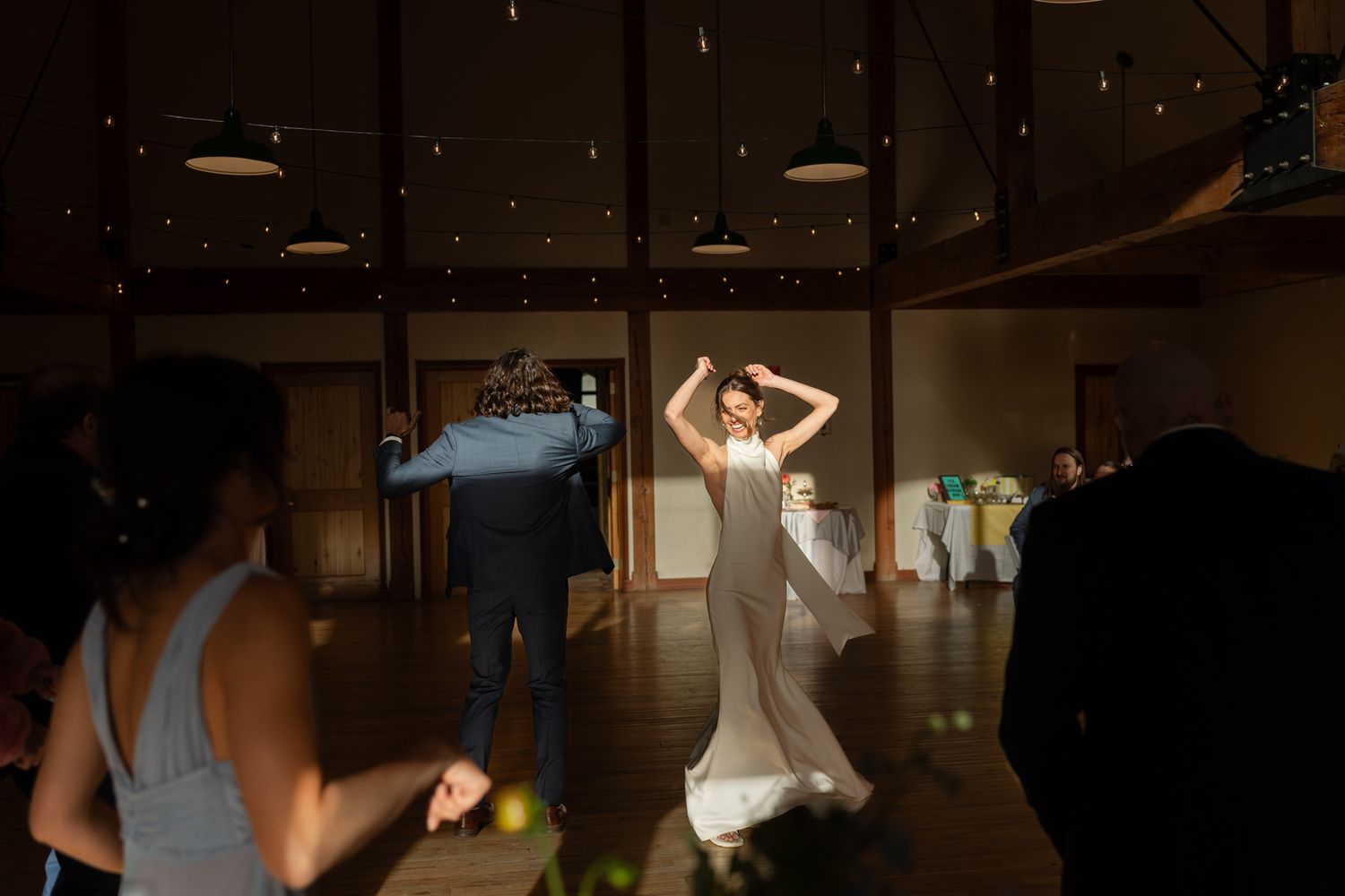 Couple dancing at a wedding reception under moody lighting and hanging pendant lamps.