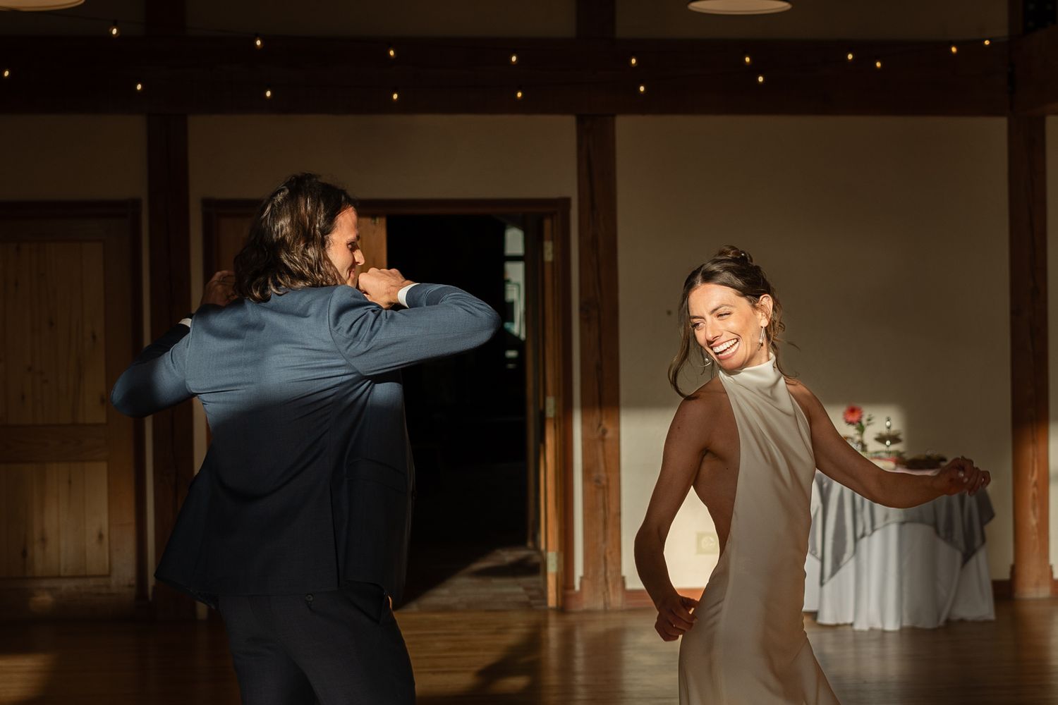 Bride and groom dancing joyfully in an indoor reception venue with ambient lighting.