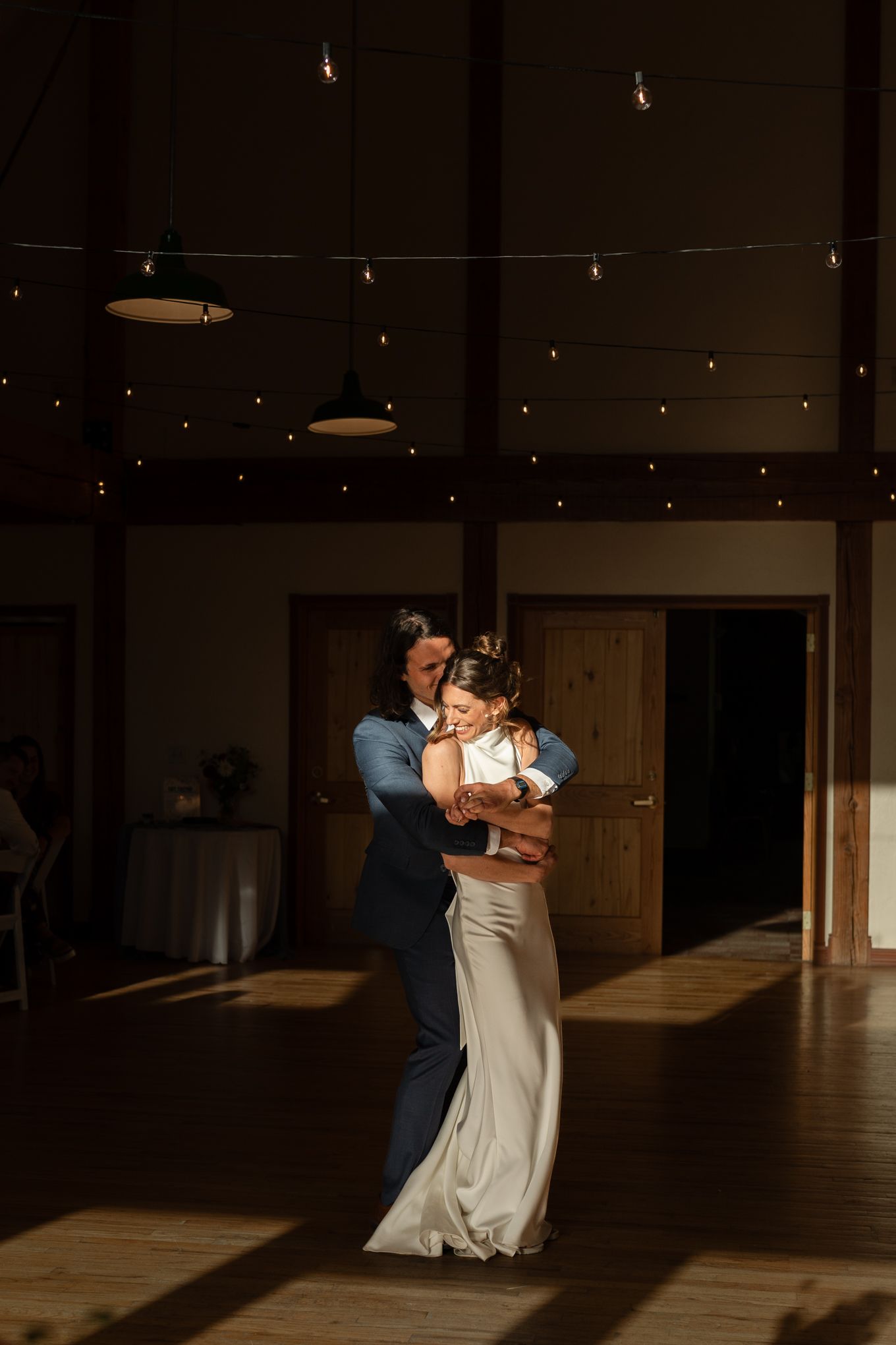 A romantic first dance moment captured in sunlit reception venue with string lights overhead.
