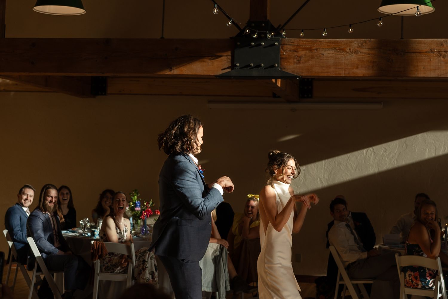 Festive dance moment at wedding reception under warm spotlights and wooden beams.