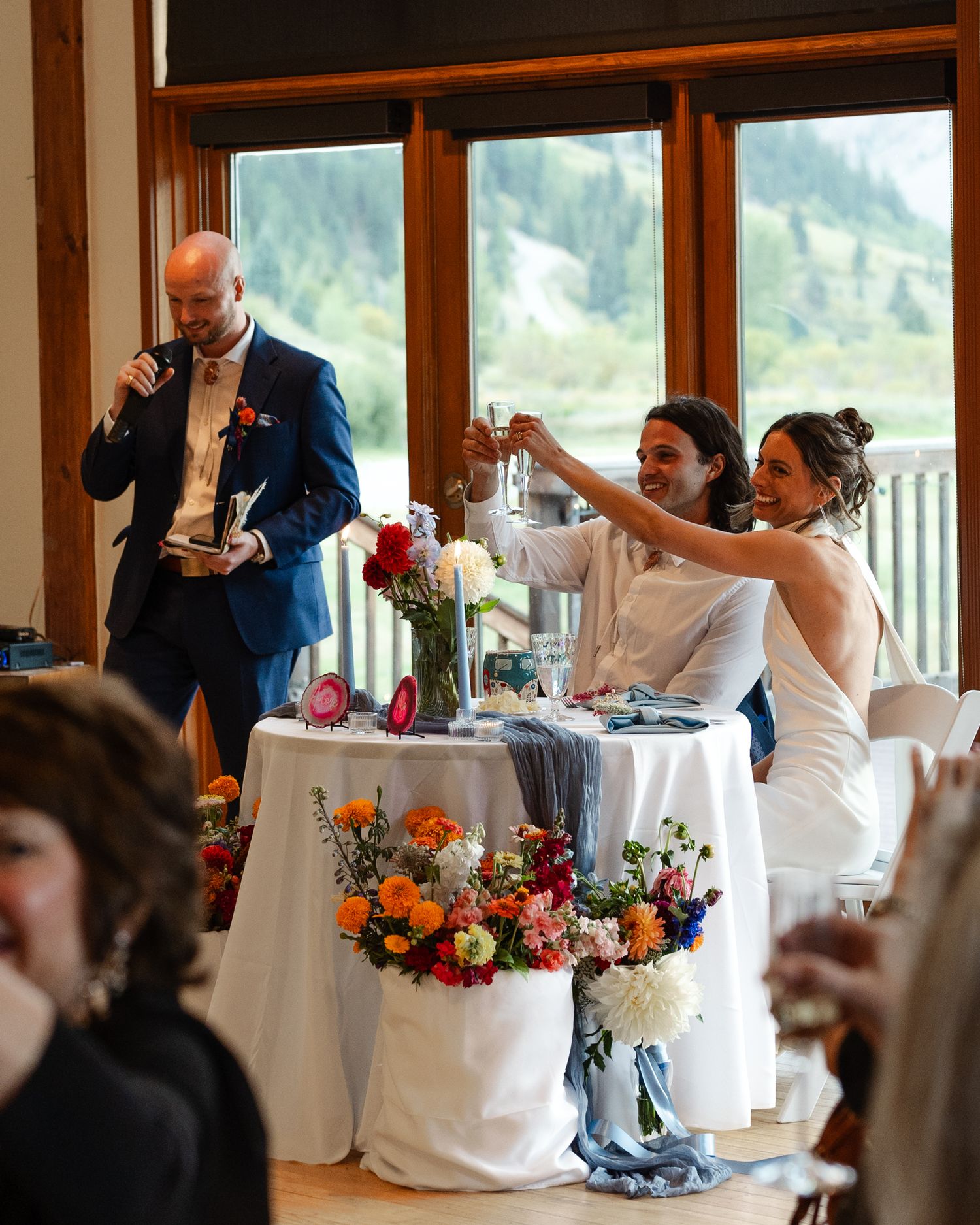 Wedding celebration with toasts and speeches at a mountain venue featuring colorful floral table decorations.