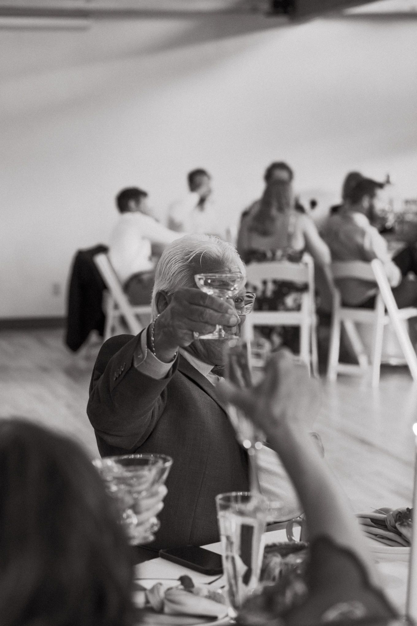 Black and white photo of a guest raising a glass during a wedding reception.