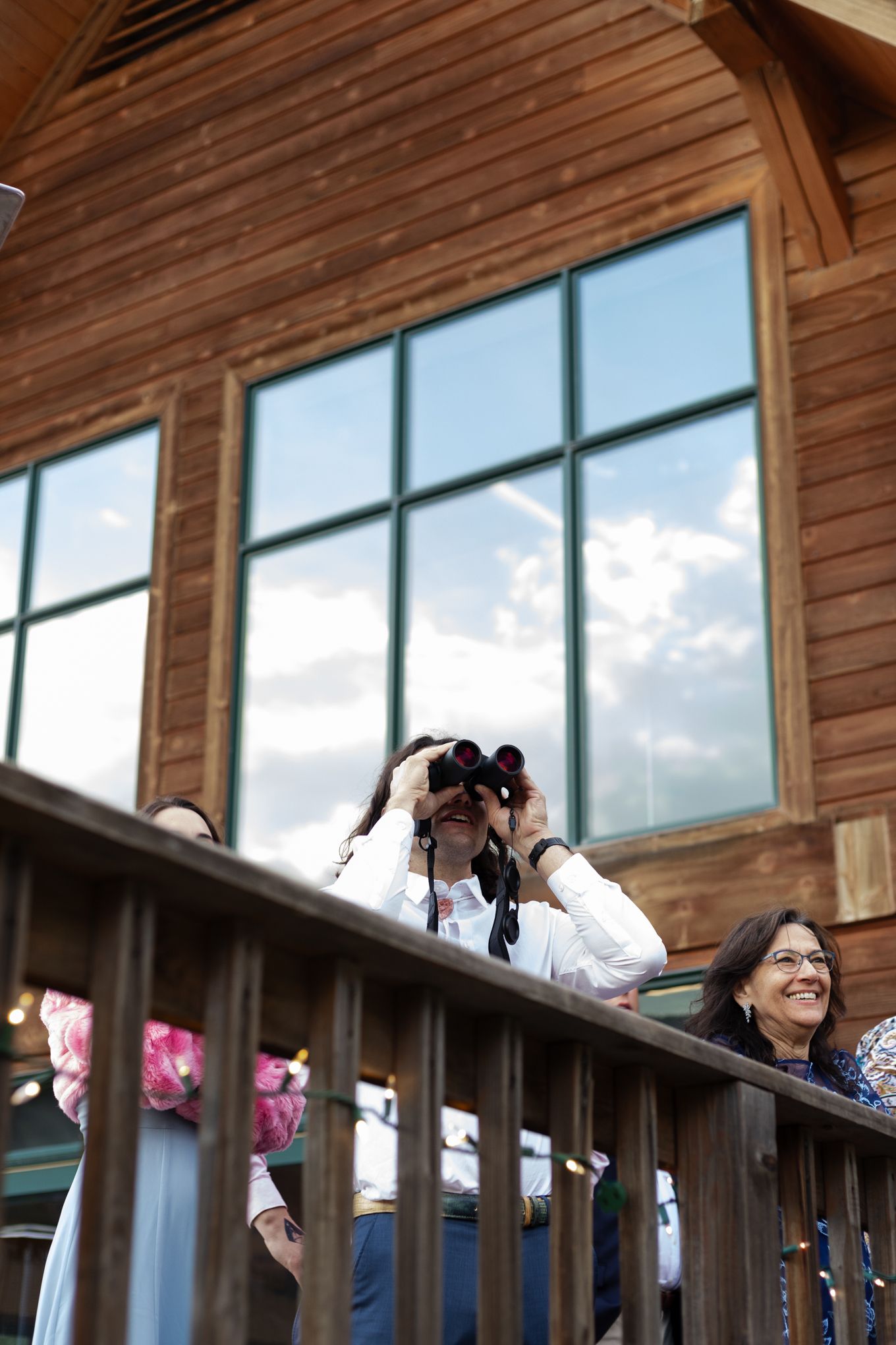 A photographer captures shots from a wooden balcony with mountains visible through large windows.