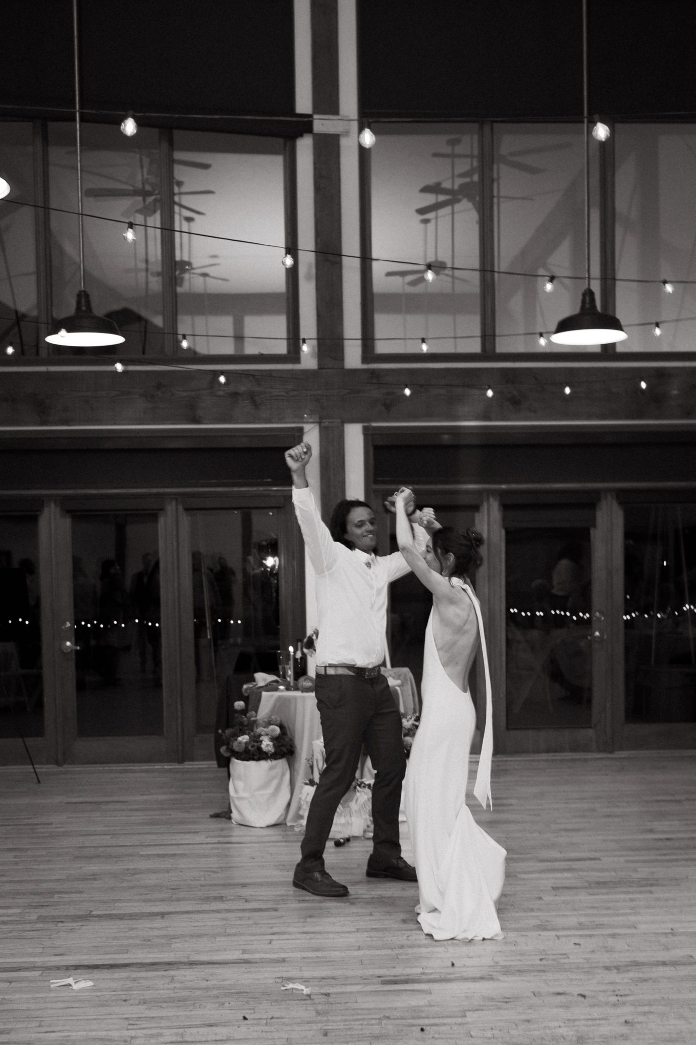 A celebratory dance moment captured in black and white on a wooden dance floor with hanging lights.
