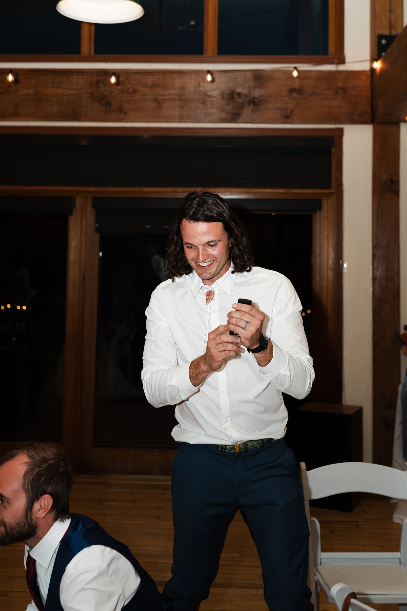 A person in a white shirt smiles while dancing at an indoor reception venue.