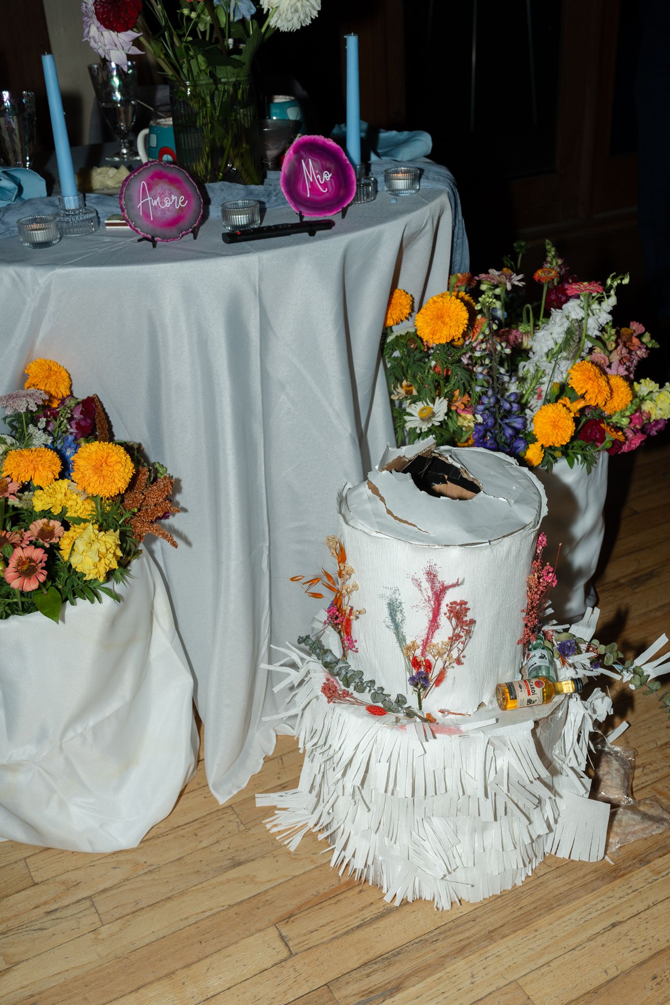 Colorful floral arrangements and a decorated cake on a white tablecloth at a celebration.
