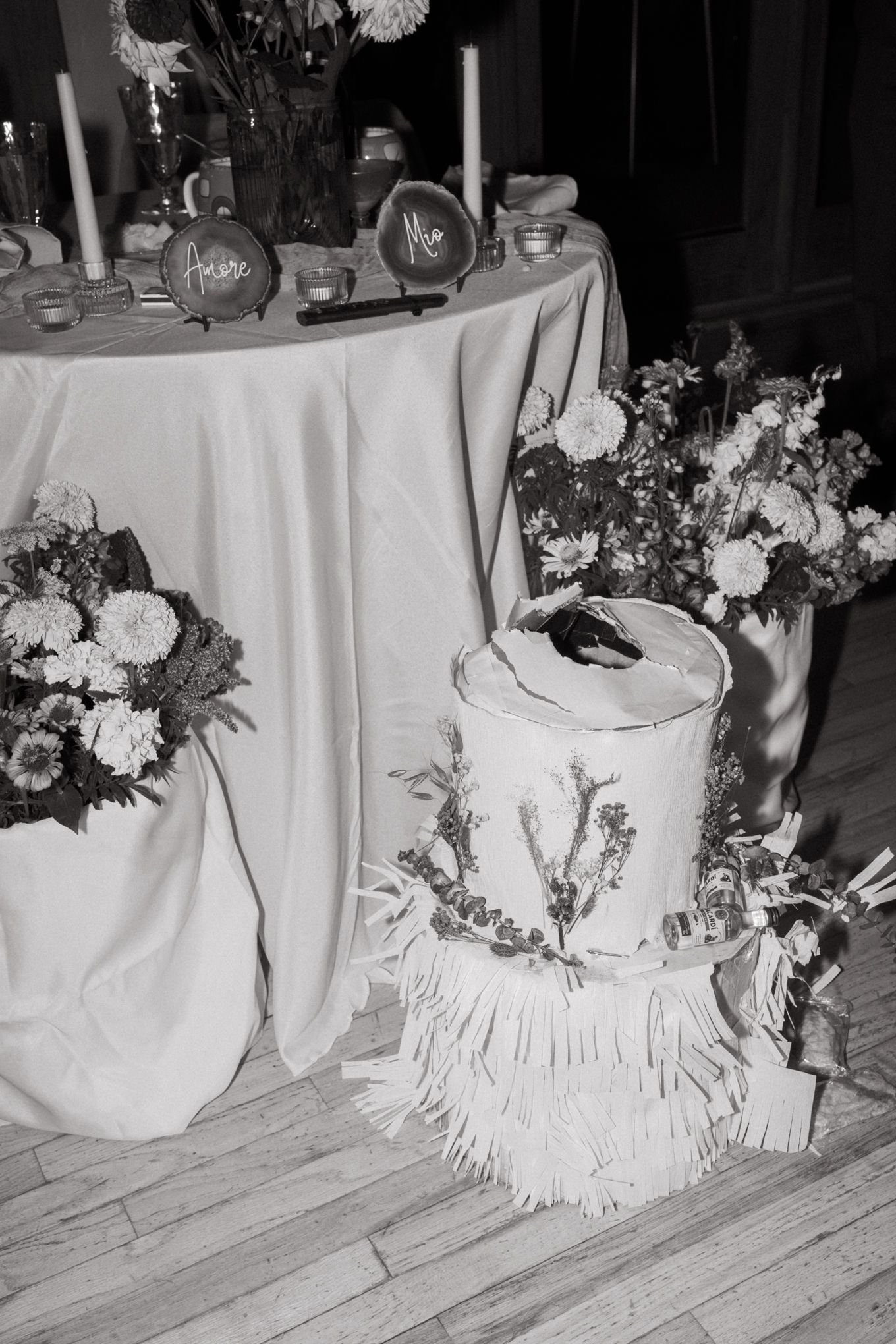 Black and white photo of an elegant wedding cake table with floral arrangements and white linens.