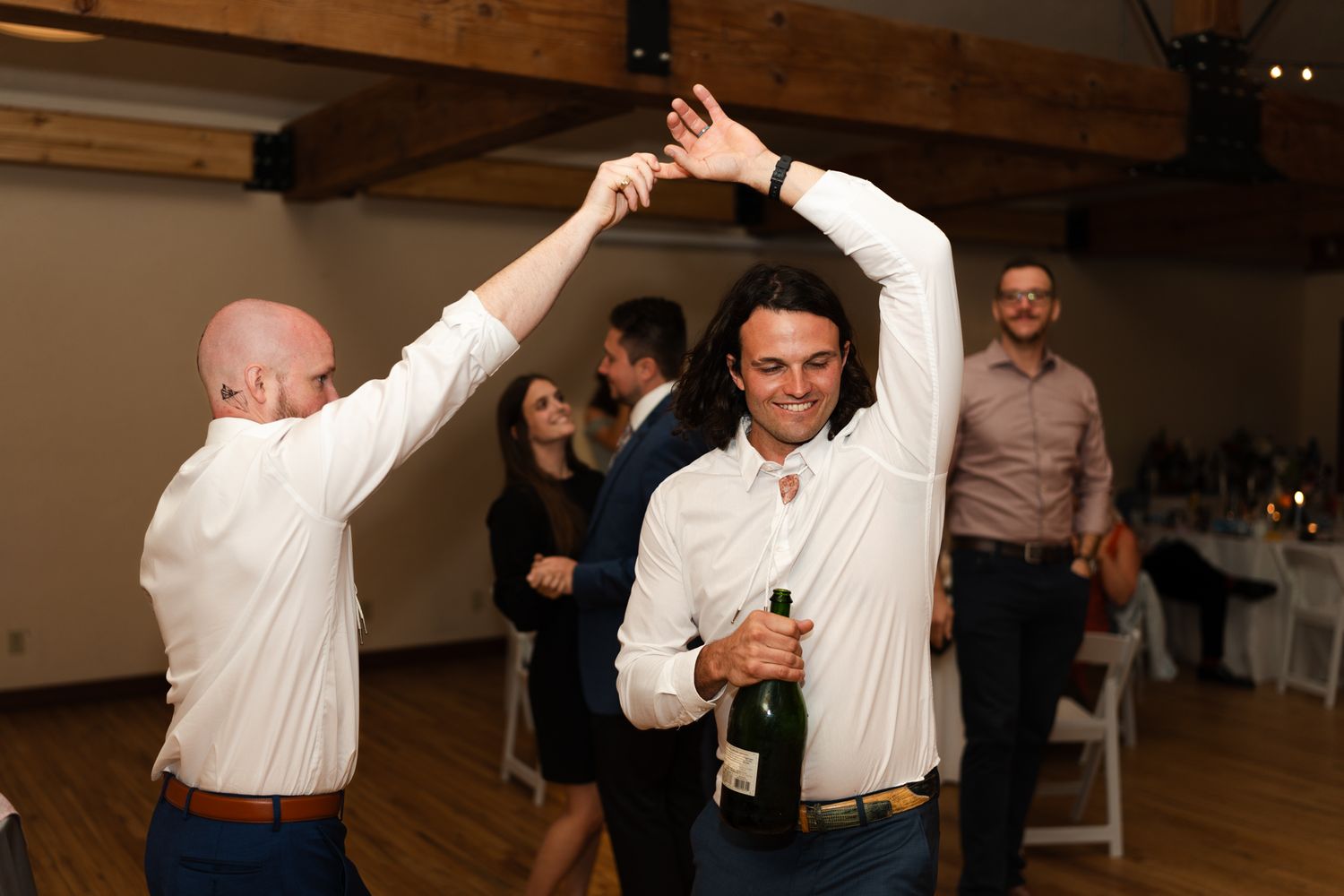 Two people dance together under wooden beams at an indoor celebration.